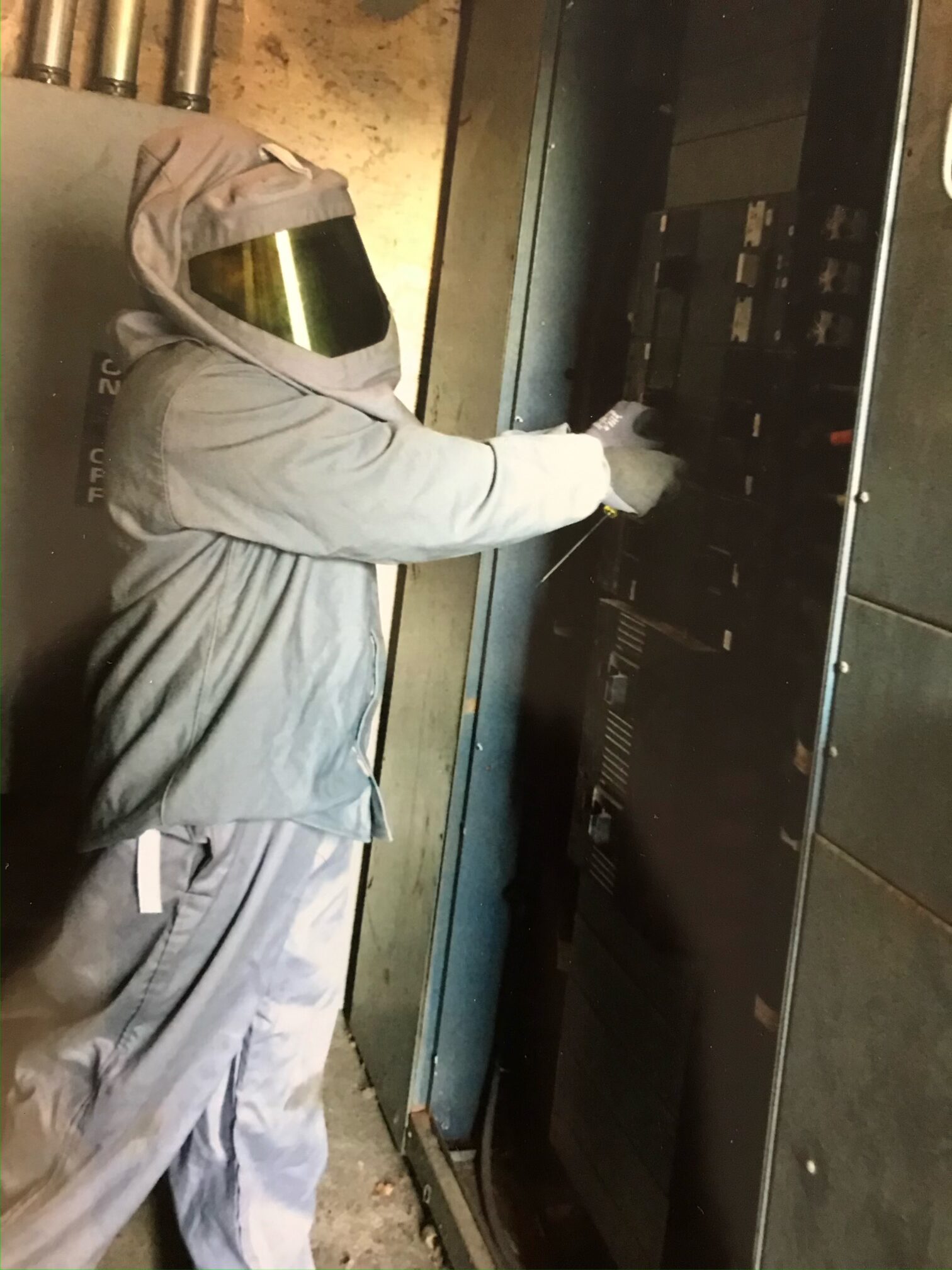 Fusion electrician in arc-flash PPE working inside an energized electrical panel